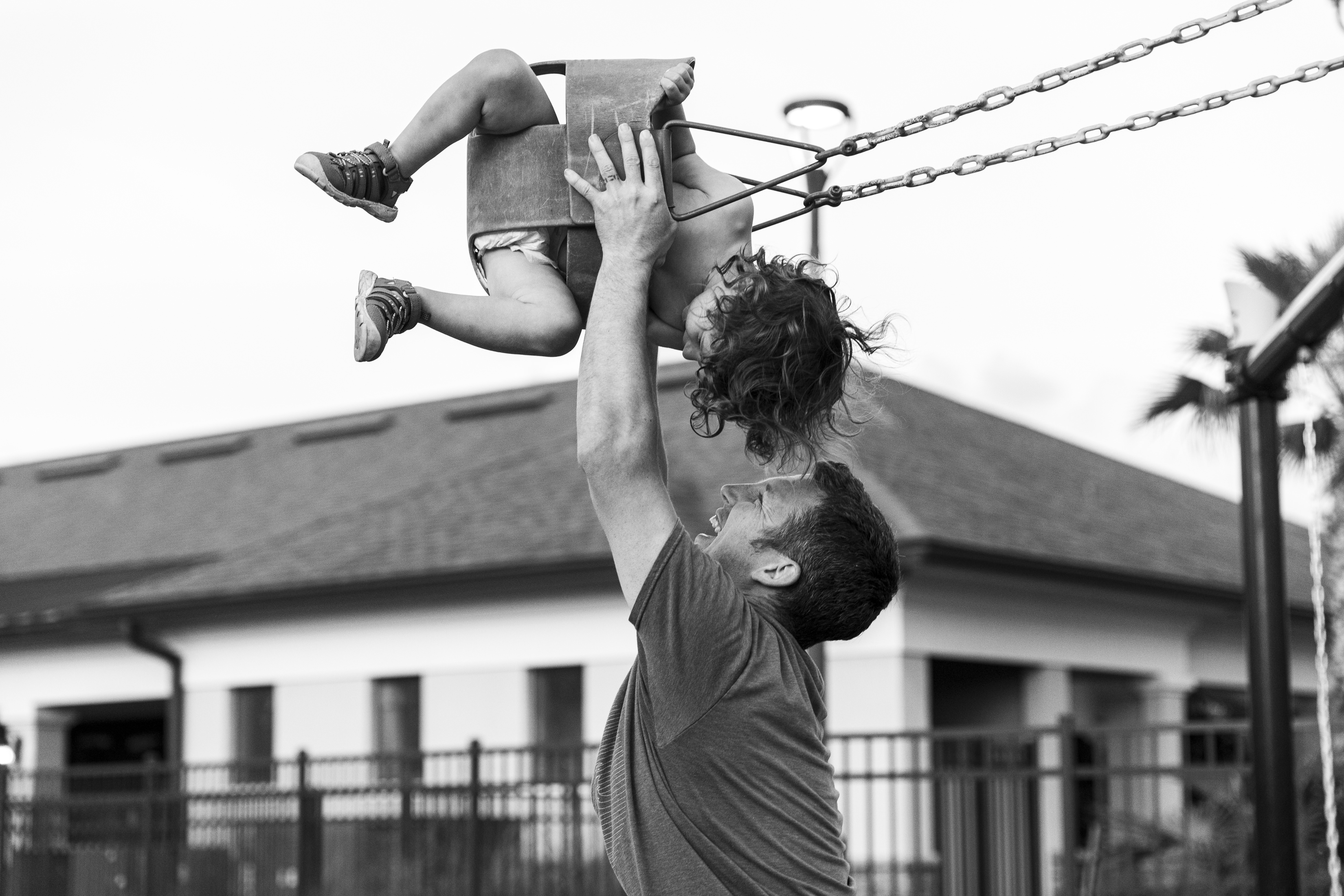 Dad holding toddler up in the swing at the park